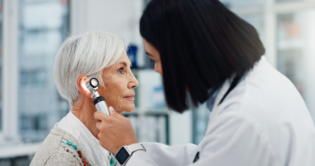 Audiologist examining a senior woman's ear with an otoscope during an on-site hearing evaluation
